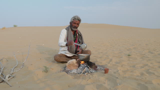 Indian man preparing chai  - masala tea, on sand dune