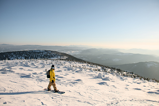 Male skier in ski clothes and equipment stands on snowcapped mountain against the backdrop of mountains and blue sky. Sunny day. Beautiful landscape at background