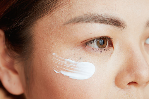 Closeup on asian woman with eye cream on face.