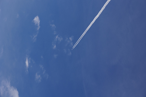 travelling with an airliner concept. close up view, looking right up at the clear sky, with a distant airplane flying and leaving behind a condensation trail