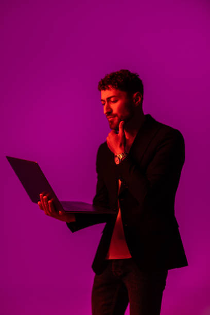 istock Work and play online. Happy man holding laptop and typing in neon light, copy space 1905195009