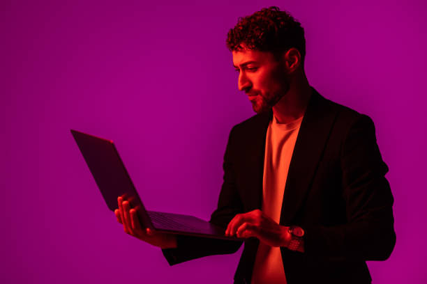 istock Work and play online. Happy man holding laptop and typing in neon light, copy space 1905197599