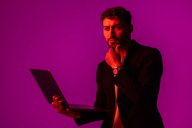 istock Portrait of man with portable computer in hand, looking at display on neon light background. 1905201776