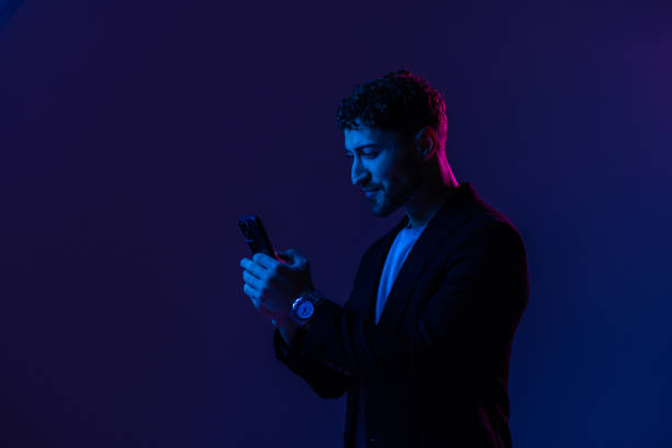 istock Man with phone in hand looking at smartphone screen, portrait dark blue background, neon light. 1905211185