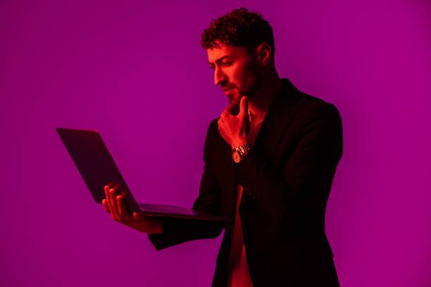 istock Portrait of man with portable computer in hand, looking at display on neon light background. 1905220851