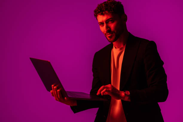 istock Work and play online. Happy man holding laptop and typing in neon light, copy space 1905222193