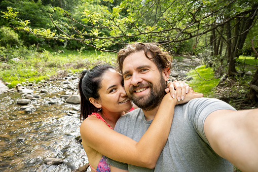 Latin couple takes a selfie on the banks of a river in Argentina. They are happy and hugged.