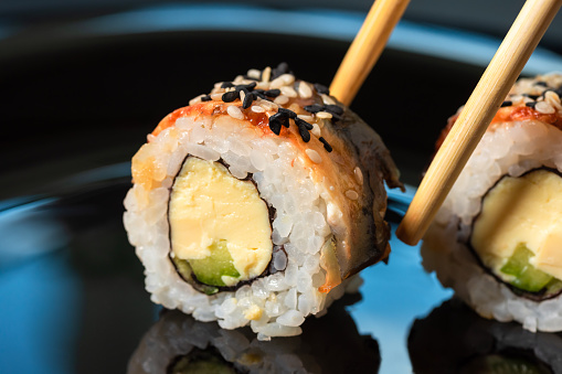 Close-up of sushi rolls with chopsticks on dark background.