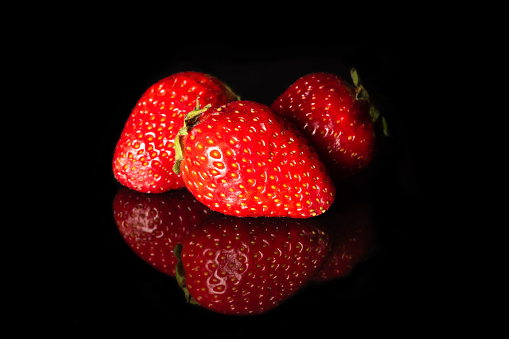 Ripe red strawberries on a black background with reflection.