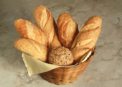Various types of breads in a wicker basket on a marble background.