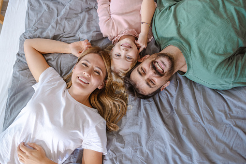 High angle shot of happy family in pajamas in bed. They are smiling and looking at the camera