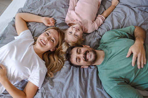 High angle shot of happy family in pajamas in bed. They are smiling and looking at the camera