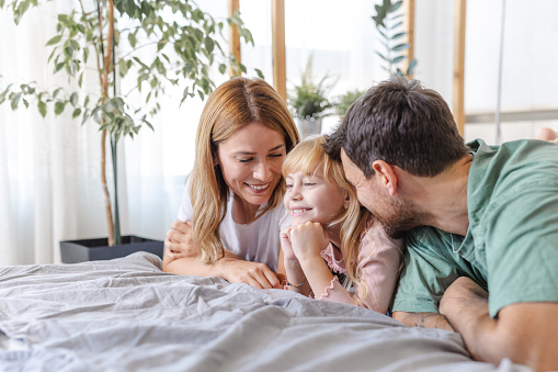 Shot of happy family in pajamas in bed. Parents are enjoying with their cute little girl