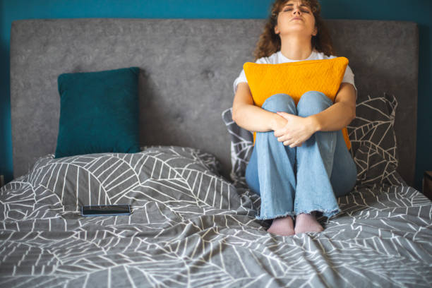 istock Depressed young woman sitting on bed hugging a pillow 1905287462
