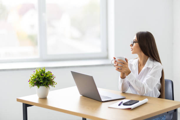istock Young businesswoman with coffee cup using phone at office 1905296777