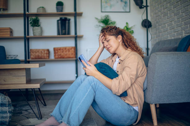 istock Depressed woman sitting on floor with mobile phone 1905306048