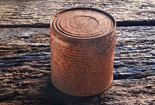 Rusty can, eight centimeters high, photographed on a rustic old wooden background. Lighting that valued the textures was used.