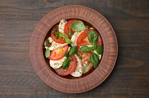 Plate of delicious Caprese salad with pesto sauce on wooden table, top view