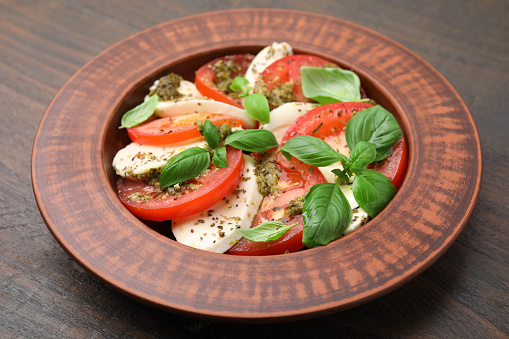 Plate of delicious Caprese salad with pesto sauce on wooden table, closeup