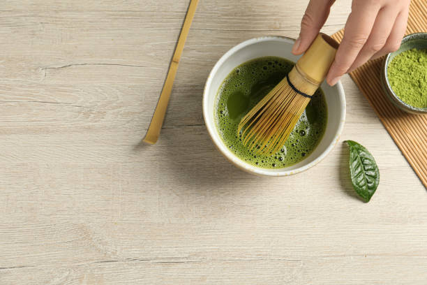 istock Woman preparing matcha tea at wooden table, top view. Space for text 1905381491