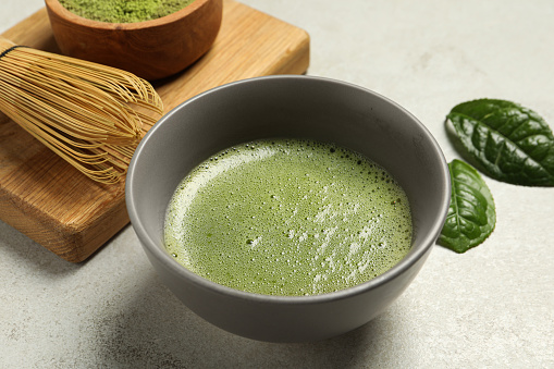 Cup of fresh green matcha tea and bamboo whisk on light grey table, closeup