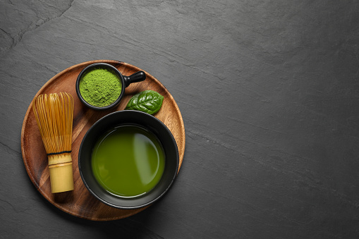 Cup of fresh matcha tea, bamboo whisk and green powder on black table, top view. Space for text