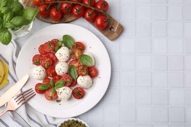 istock Tasty salad Caprese with tomatoes, mozzarella balls and basil served on white tiled table, flat lay. Space for text 1905396985