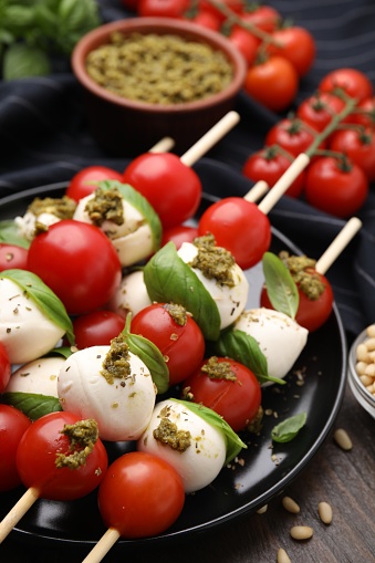 Caprese skewers with tomatoes, mozzarella balls, basil and pesto sauce on table, closeup