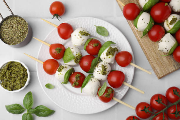 istock Caprese skewers with tomatoes, mozzarella balls and basil on white tiled table, flat lay 1905402723