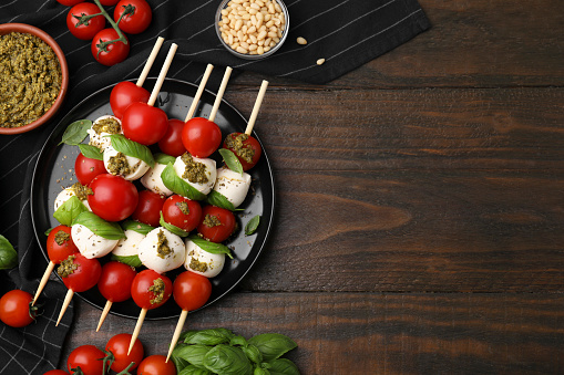 Caprese skewers with tomatoes, mozzarella balls and basil on wooden table, flat lay. Space for text