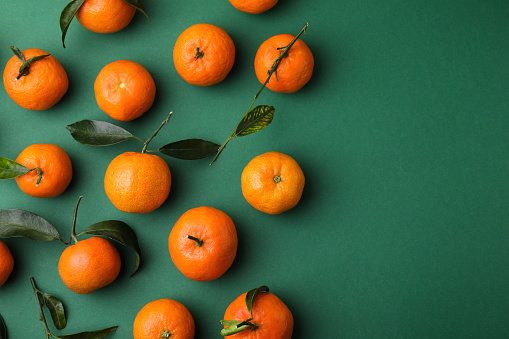Fresh ripe tangerines with leaves on green background, flat lay. Space for text