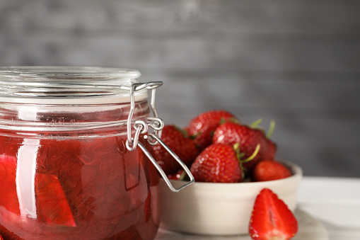 Jar of tasty rhubarb jam and strawberries on white table, closeup. Space for text