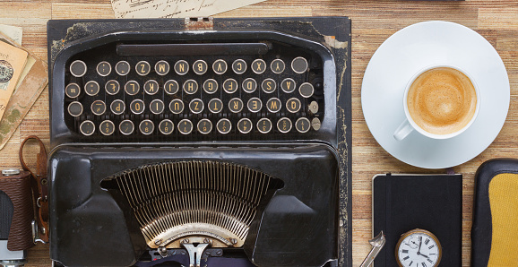 black retro typewriter with cup of coffee on wooden table, top view