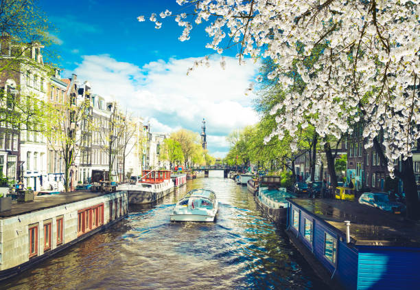 Facades of dutch houses over canal with floating boat, Amsterdam spring scenery, Netherlands