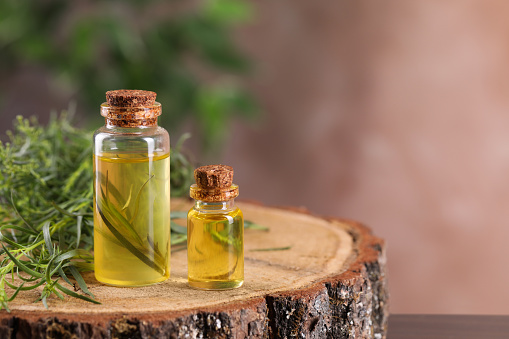 Bottles of essential oil and fresh tarragon leaves on wooden stump. Space for text