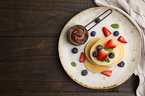 Delicious pancakes served with berries and chocolate spread on wooden table, top view. Space for text