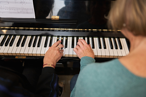 Rear view of two mature women at home playing the piano together and singing. Hobby, vocal and musicianship, piano lessons for adults.
