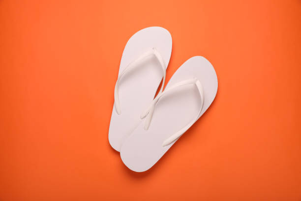 istock Stylish white flip flops on orange background, top view 1905517267