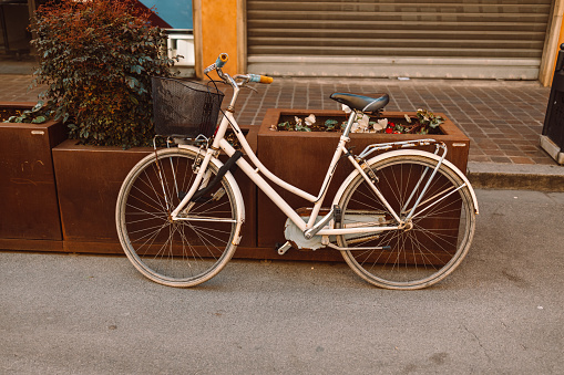 Old bicycle parked on a street in Valencia, Spain. An white bicycle near a flower bed in the center of a strictly urban area