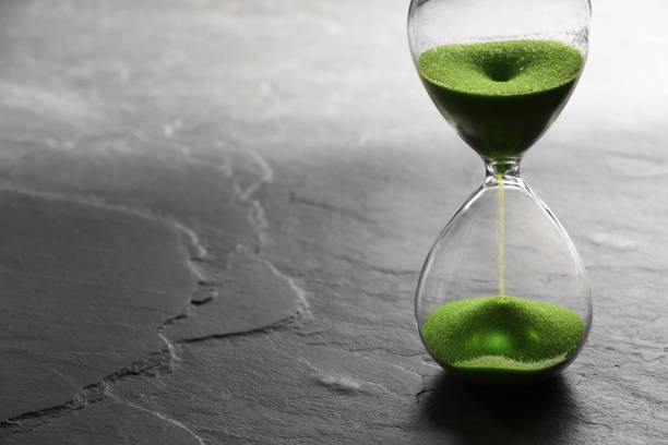 istock Hourglass with light green flowing sand on black table. Space for text 1905539950