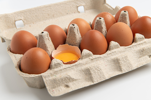 Eggs tray with brown eggs. One eggshell broken. Yellow egg yolk