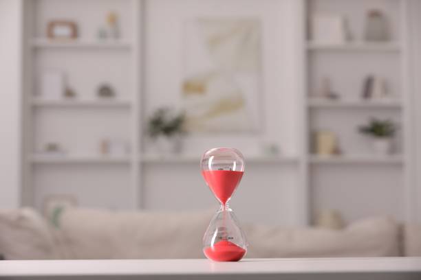 istock Hourglass with red flowing sand on white table against blurred background 1905580048
