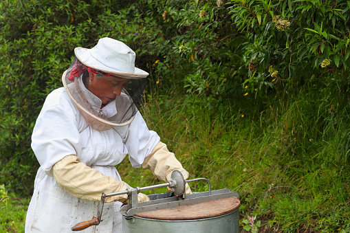 Latina beekeeper placing the lid on the honey extractor, with a natural background, dressed in a white protective suit