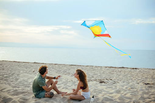 Happy couple playing with kite on beach near sea.