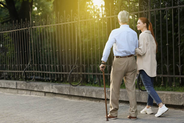 istock Senior man with walking cane and young woman outdoors, back view. Space for text 1905691268
