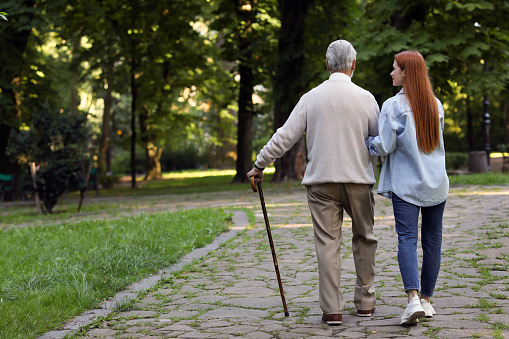 Senior man with walking cane and young woman in park, back view. Space for text