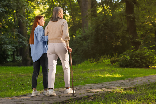 Senior lady with walking cane and young woman in park. Space for text