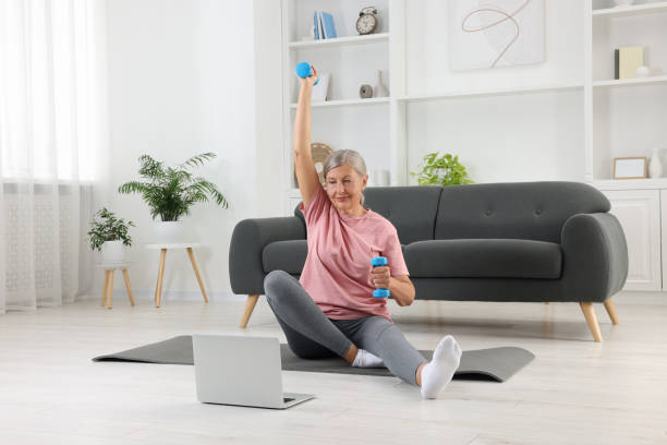 istock Senior woman exercising with dumbbells while watching online tutorial at home. Sports equipment 1905727261