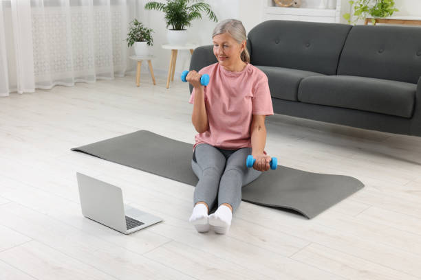 istock Senior woman exercising with dumbbells while watching online tutorial at home. Sports equipment 1905727380