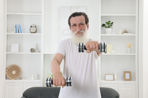 Senior man exercising with dumbbells at home. Sports equipment